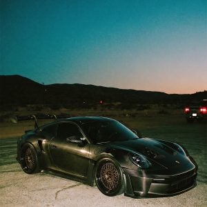 Porsche 911 with a carbon-fiber exterior and bronze-toned Klutch mesh wheels, viewed from the front three-quarter angle at dusk