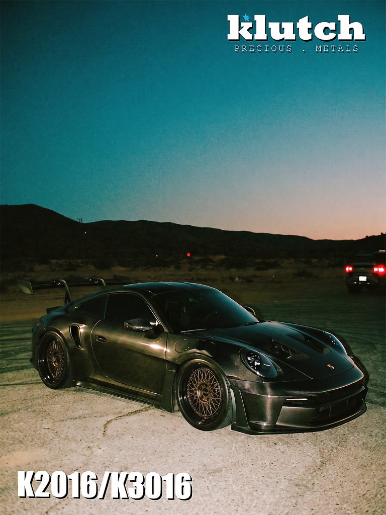 Porsche 911 with a carbon-fiber exterior and bronze-toned Klutch mesh wheels, viewed from the front three-quarter angle at dusk
